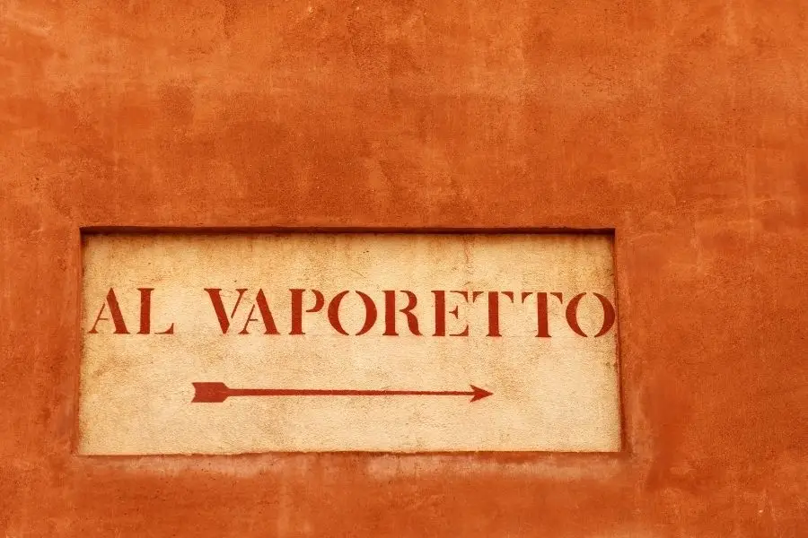 A painted 'Al Vaporetto' wall sign with an arrow pointing to the water-bus stop in Venice