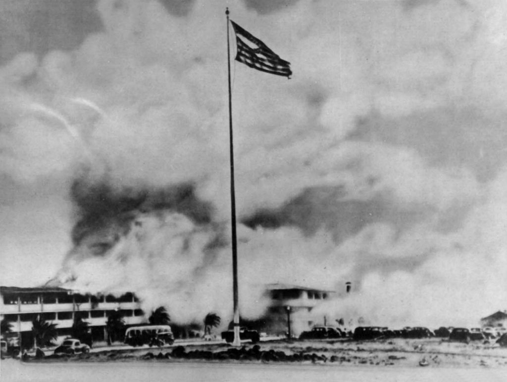 Burning barracks and shredded American flag at Hickam Field on December 7, 1941