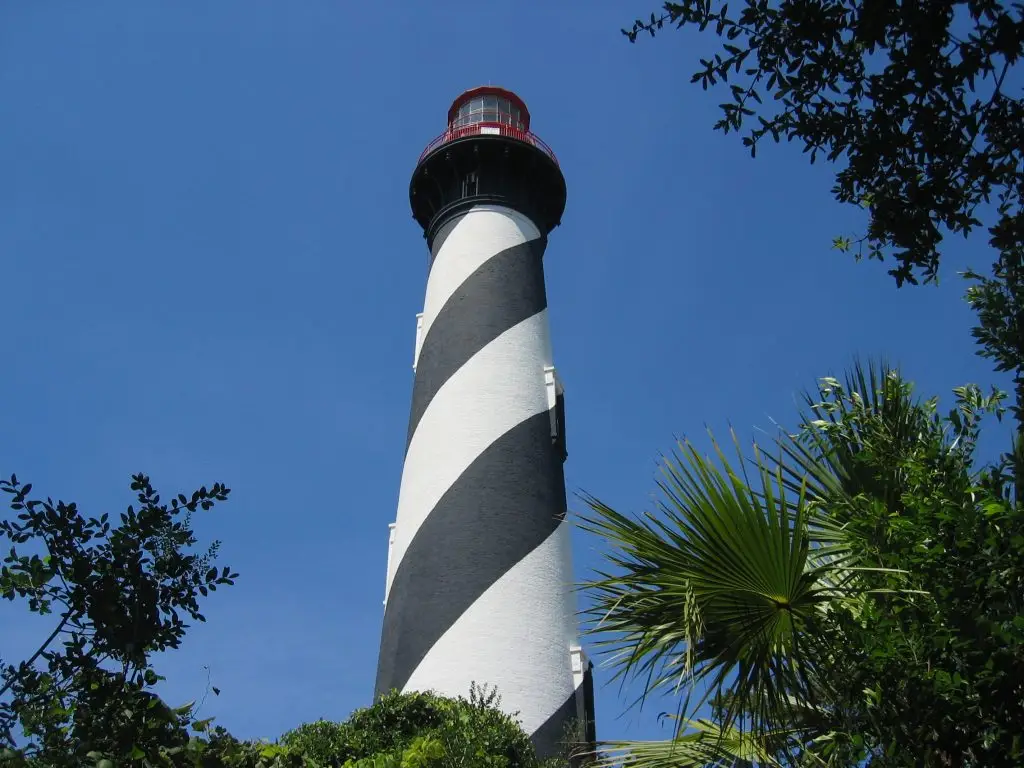 The black and white spiral St. Augustine Lighthouse rising above palms and oaks against a deep blue sky